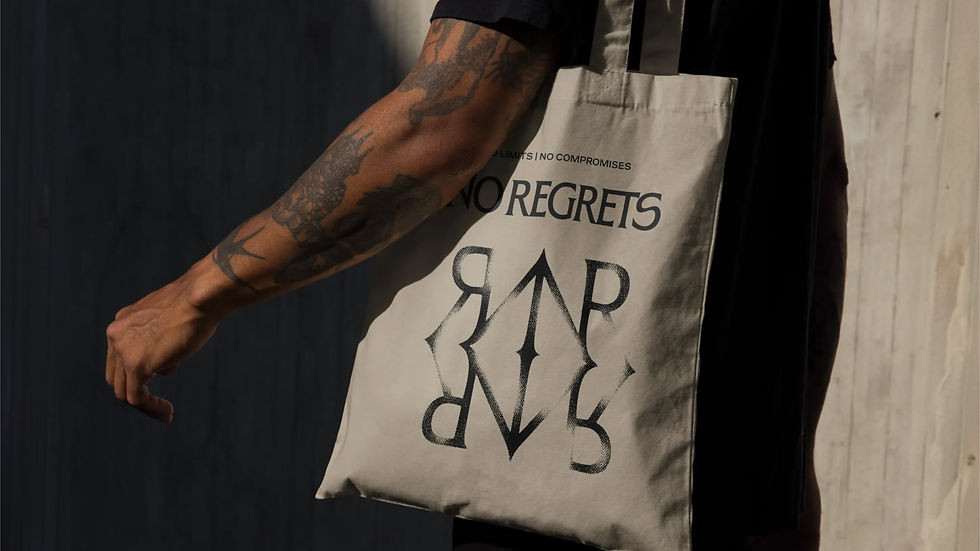 Tattooed person carrying a canvas tote bag featuring the No Regrets logo and monogram.