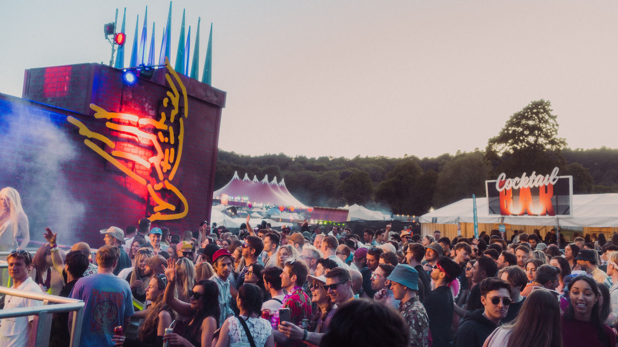 Shambarber stage - a brick column with artwork of an abstract dancing figure in yellow, the crowd standing in front and a cocktail bar to one side.