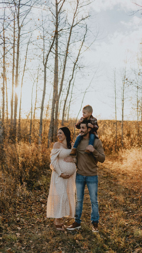 Fall Photos outside with family of three dad with son on his shoulder and mom in a maternity gown with her growing belly photo by Alte Studios from North Battleford Saskatchewan