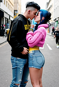 punk_girl_wearing_yellow_croptop_blueshorts_and_sneakers_snogging_a_young_man_wearing_swea