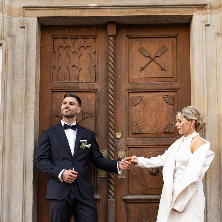 Brautpaar steht vor historischer Holztür – elegante Hochzeitsaufnahme