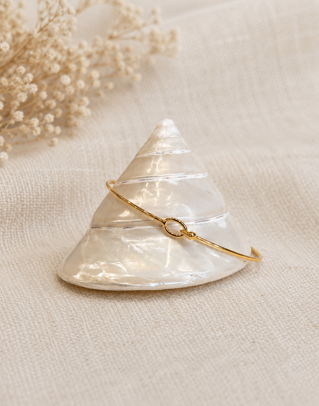 Bracelet doré posé sur un coquillage blanc