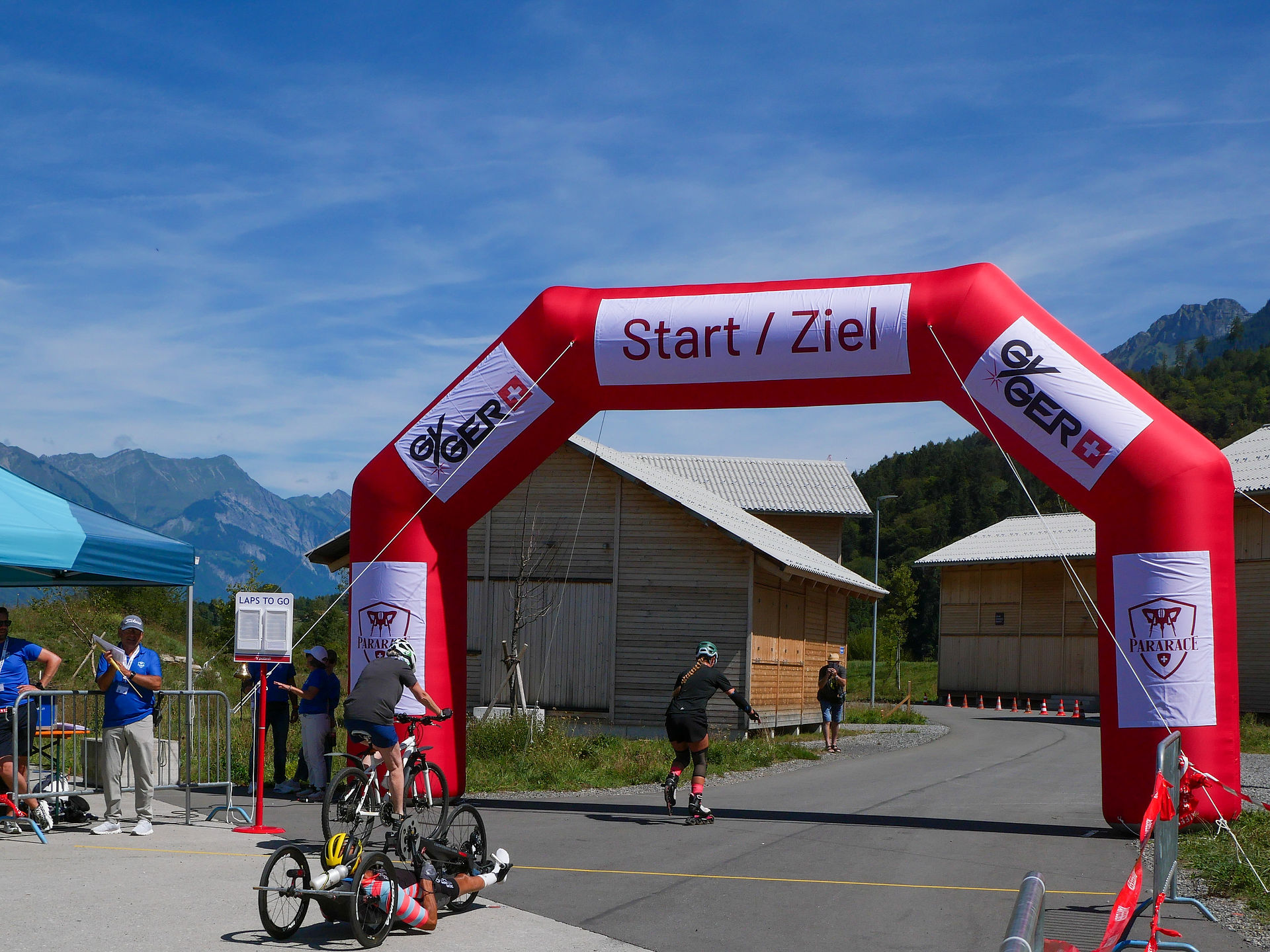 Teilnehmende auf Inline Skates, dem Velo und im Handbike passieren gemeinsam den Start und Zielbogen