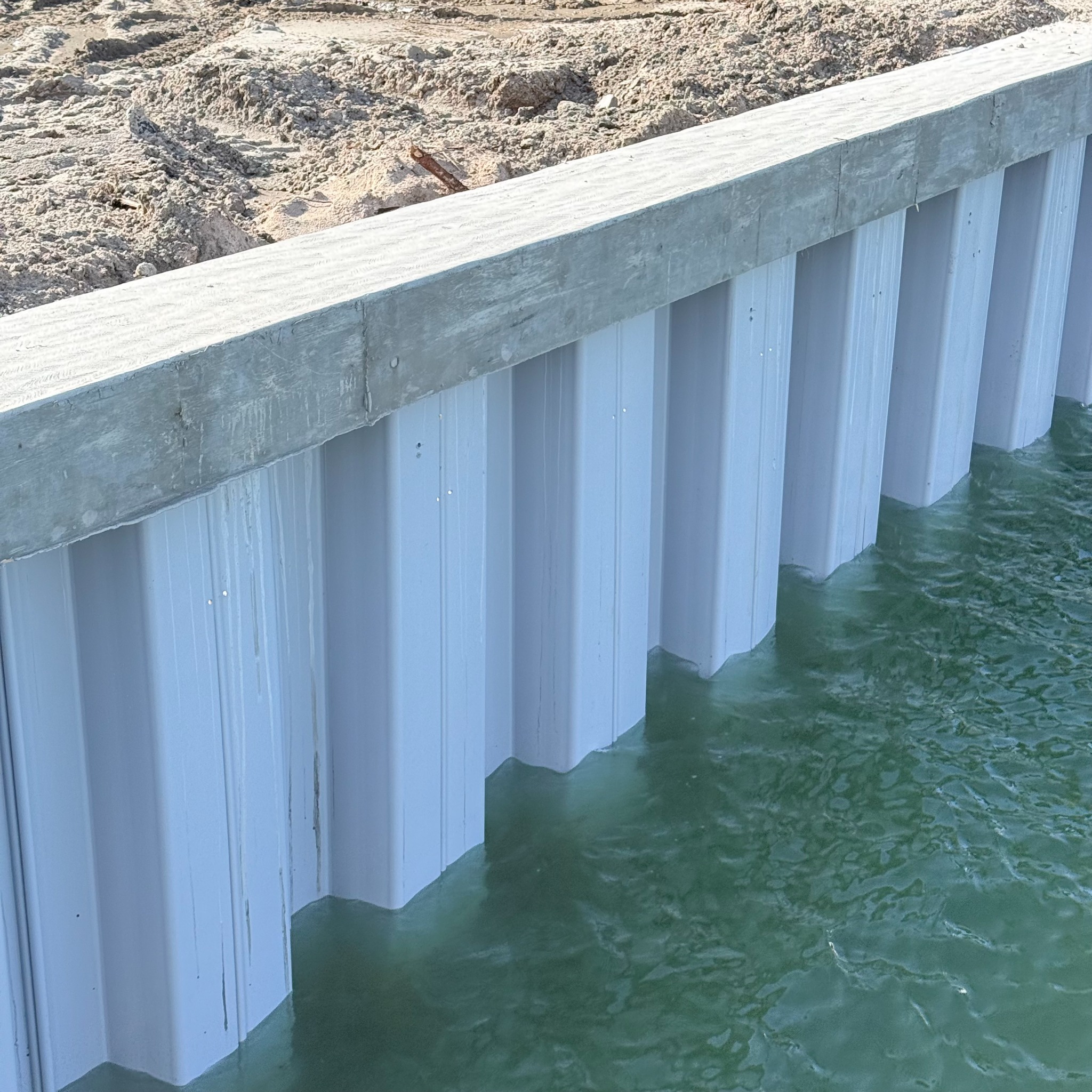 Close view of white vinyl seawall panels beneath a concrete cap