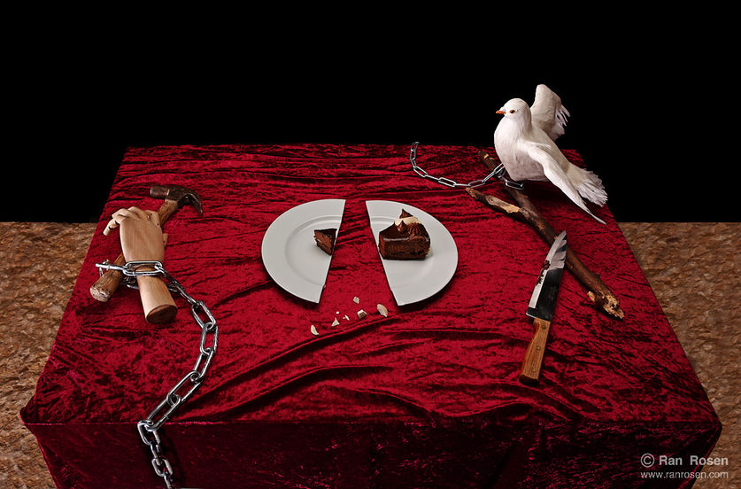 A still-life composition on a red velvet-covered surface featuring a plate with a missing slice of cake, a mannequin arm wrapped in metal chains on the left, and a white dove on the right beside wooden sticks and a knife. A metal chain runs across the scene.