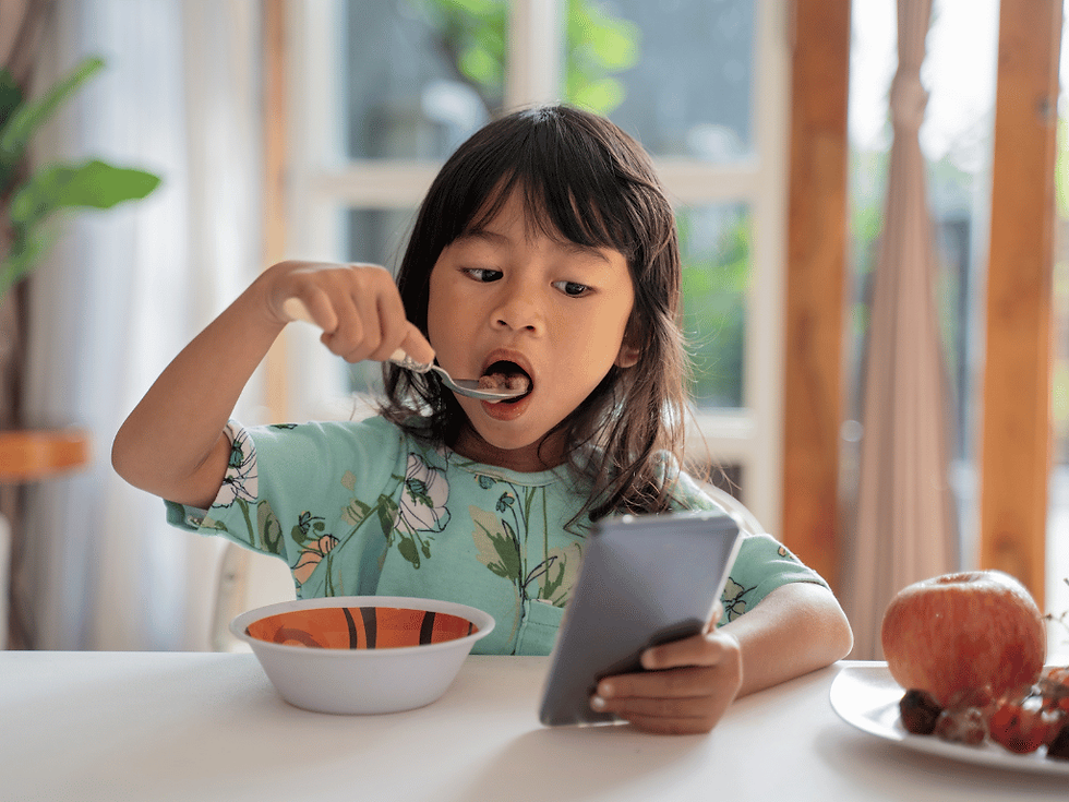 Young girl eats cereal while looking at a smartphone.