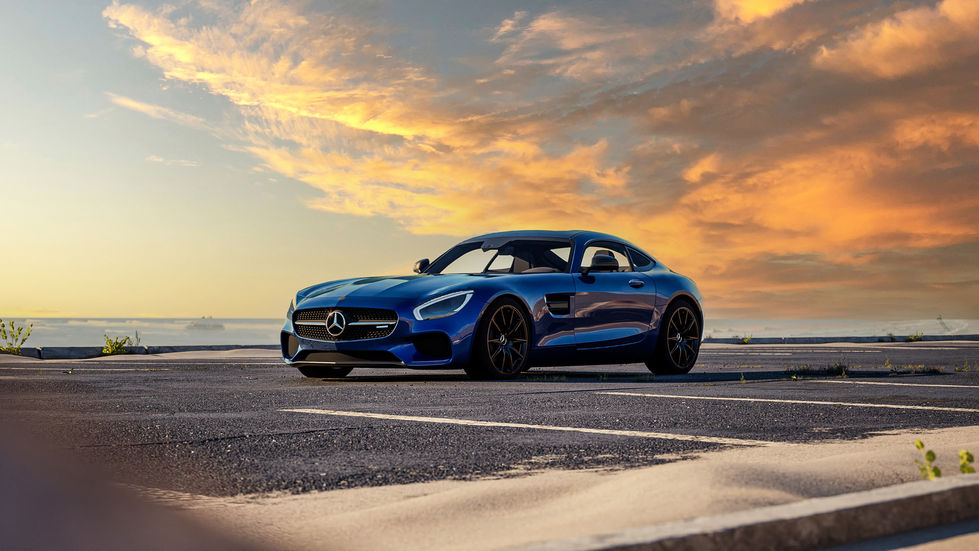 Mercedes-AMG GT in vibrant blue parked in an empty lot during a picturesque sunset, showcasing its sleek design and performance-oriented aesthetic.
