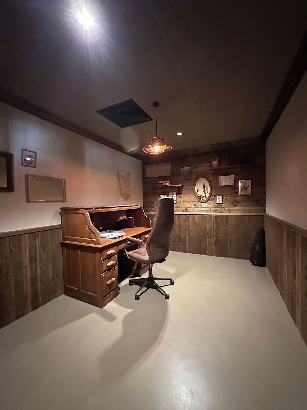 Bureau d’O’Fun Park avec canapé en cuir, fauteuil de travail, boiseries et sol beige en béton ciré.