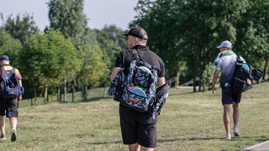 Diskgolfo diskai, kuprinės, žaidėjai nešasi ant pečių ir žaidžia, aktyviai