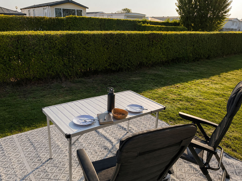 Campingtisch mit Notizbuch, Trinkflasche und Snack auf einem Campingplatz.