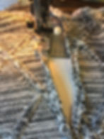 Close-up of a sewing machine stitching gray patterned fabric. The needle moves along a textured seam, creating detailed woven patterns on sweater knit fabric.