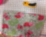 Image of a piece of fabric with a playful ladybug and butterfly design on a light gray background, laid flat on a cutting mat with grid lines. A yellow rotary cutter is placed above the fabric, ready for cutting.