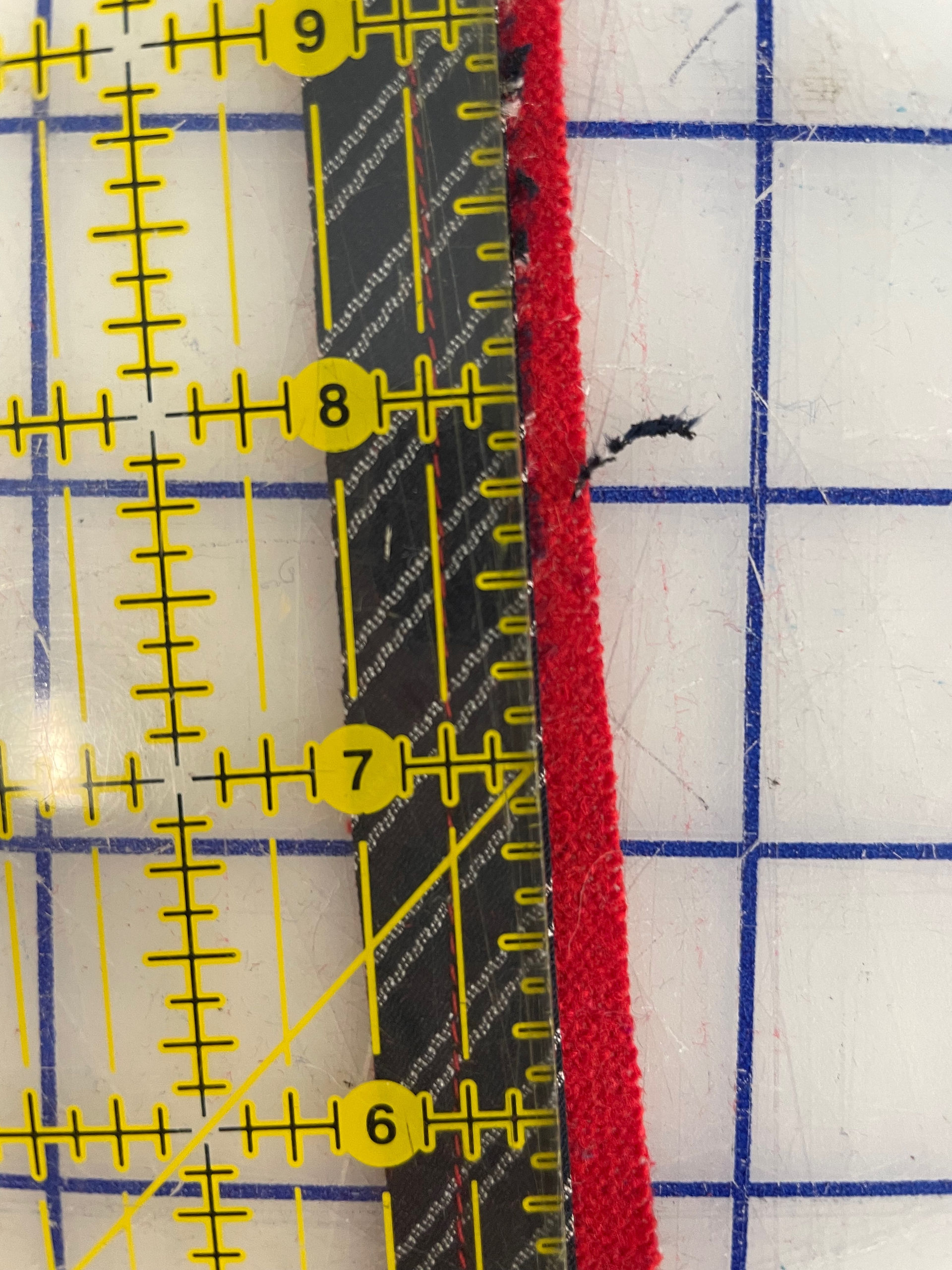 A close-up view of a USA Collection fabric piece, featuring red and black striped material, measured against a quilting ruler with yellow and black markings on a blue and white grid cutting mat, used for precise crafting and sewing