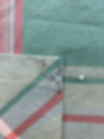 Close-up of pinned green and red striped fabric, with visible stitching and lines. The setting is on a textured surface.