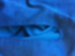 Close-up of blue fabric with a slit showing a textured, dotted pattern underneath. The fabric has a soft, calming appearance. Demonstrates stay stitching to stabilize an armhole for the super simple circle cape.