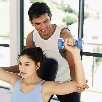 personal trainer helping woman do a dumbbell shoulder press