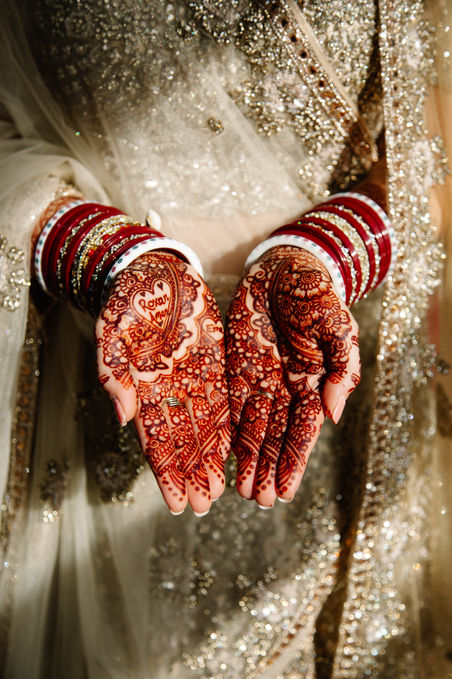 Bridal mehndi with groom’s name hidden in henna design during Sikh wedding - red bangles and gold sari captured in cinematic detail by Noelle Vaughn Wedding Photography.