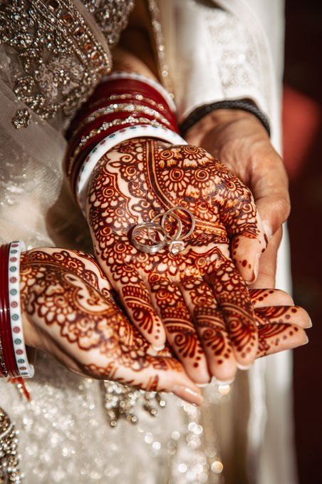 Sikh bride holding wedding rings in henna-decorated palms with red bangles and gold embroidery - fine art wedding detail photography by Noelle Vaughn.