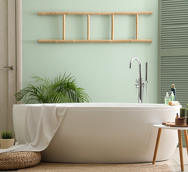 Interior of bathroom with modern bathtub, bath accessories and houseplants near green wall