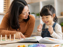 A mother helps her child practice blending sounds while reading a children’s book at home.