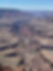 A wide aerial view of a deep canyon with layered red and brown rock walls and a turquoise river winding through the bottom, showing the vast scale and rugged beauty of the landscape.