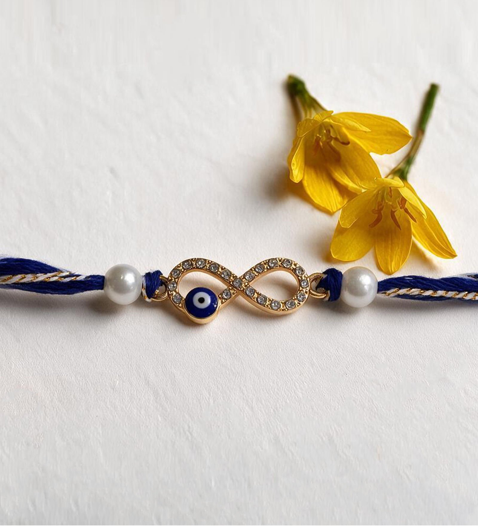 Handmade Infinity Evil Eye Rakhi with Crystal Stones, Pearl Beads & Blue Cotton