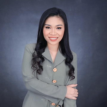 Professional Asian woman with long black curly hair wearing a green blazer, smiling confidently in front of a dark studio bac
