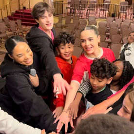 Diverse group of kids and adults with hands joined in huddle.
