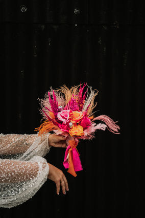 bride holding bouquet of hot pink and orange flowers with feathers