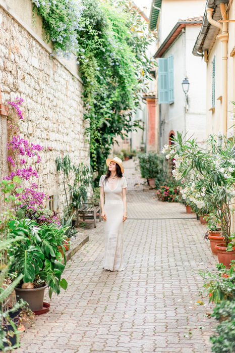 Anca Lungu walking alone in a charming street in Villefranche-sur-Mer, with beautiful flowers and pastel-colored buildings.