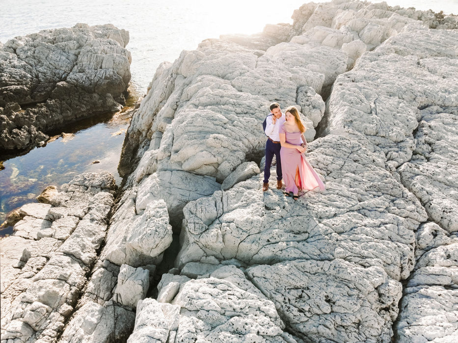 Aerial drone photo of a couple embracing on rocky beach shore, captured on the French Riviera by The Bercans.