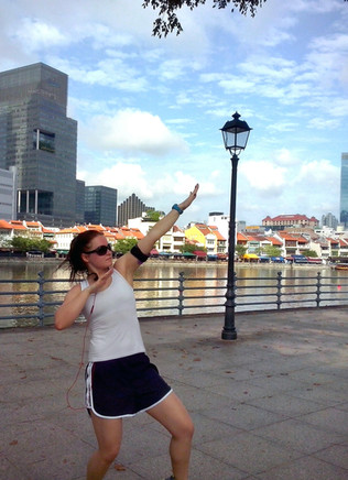 A woman in a white athletic top and black running shorts outdoors by the river posing.