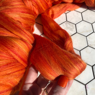 Orange combed wool in fingers with orange nails painted