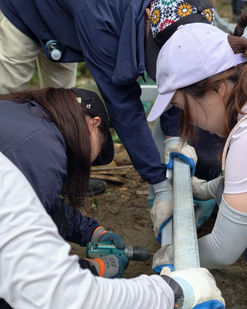 Volunteers working together to drill and assemble materials for a rural bridge repair project.