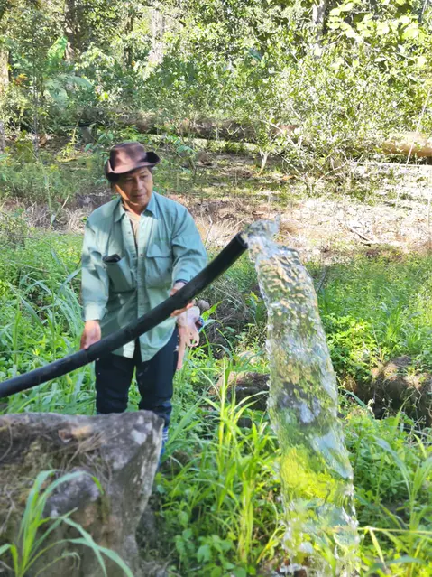 Rural villager holding a water pipe with clear, steady water flow after the gravity water project.