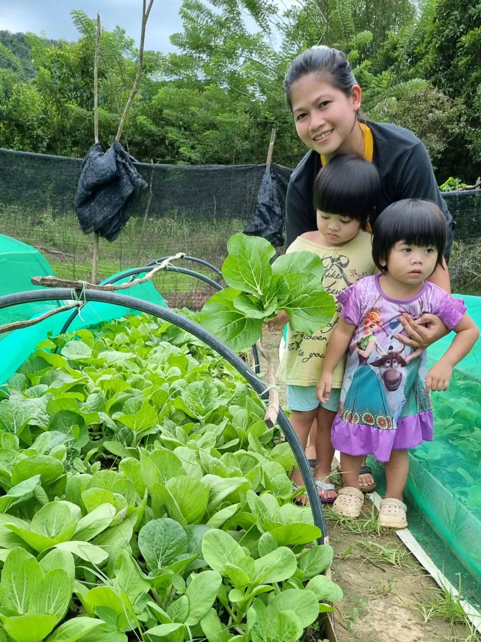 farmer with her children & her farm filled with blooming and organic vegetables.webp