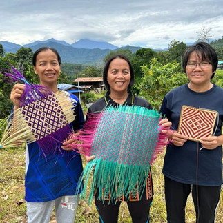 Three of our rural women beneficiaries smiling as they hold the half finished crafts they made