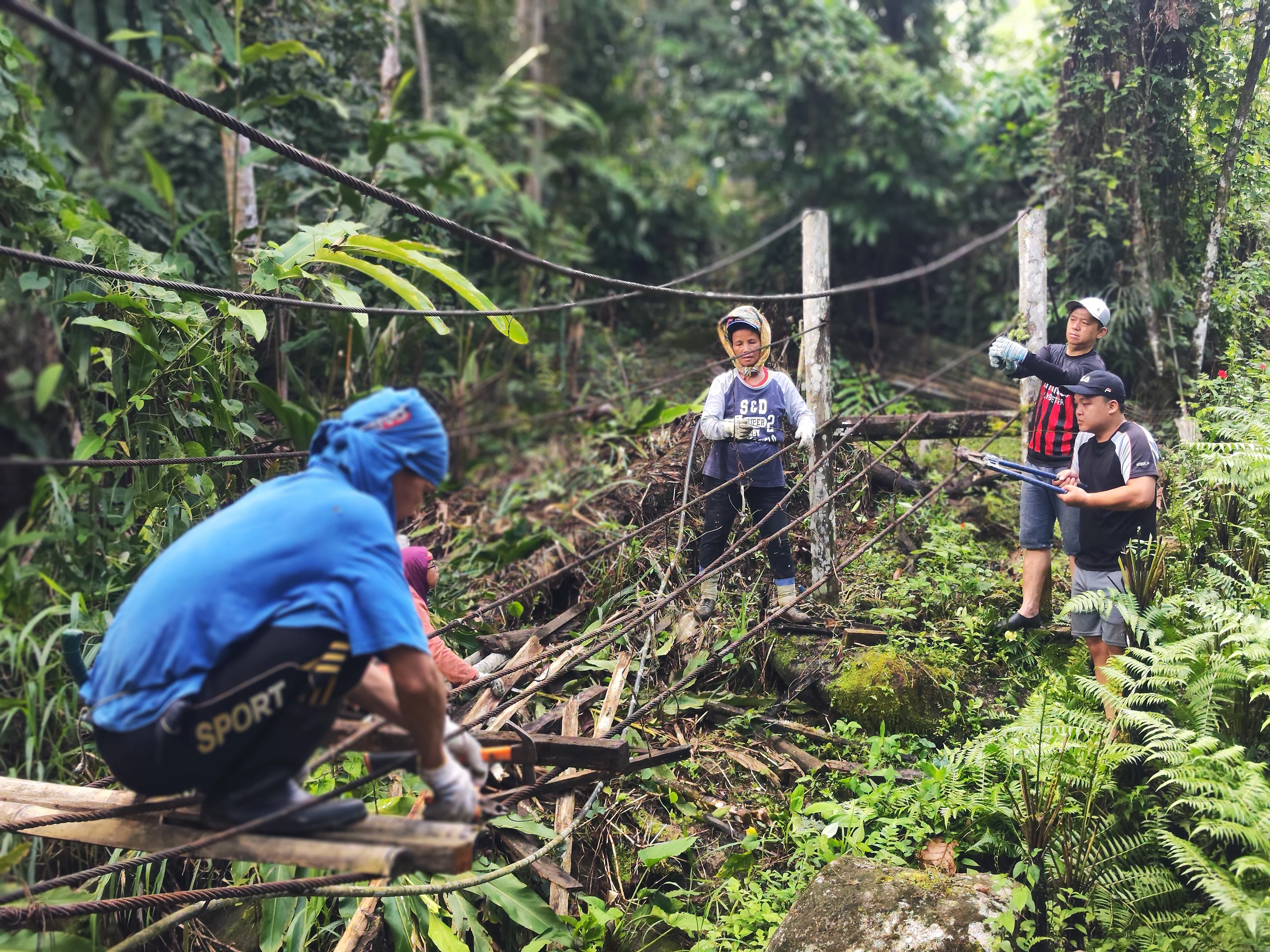 villagers working together to remove broken, rusted materials from the old bridge