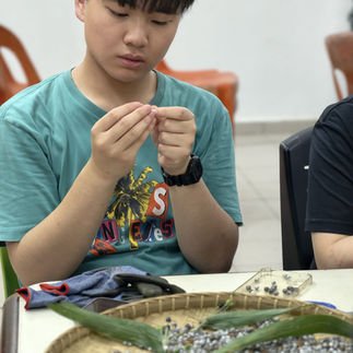 Volunteer creating a bracelet using locally sourced materials like "dalai".
