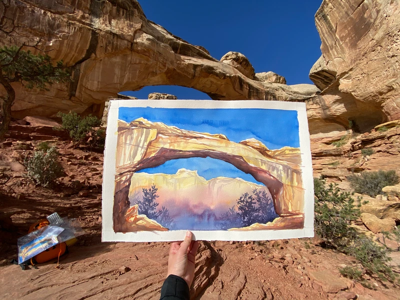 photo of a large watercolor showing a sandstone bridge in front of the landscape that was painted