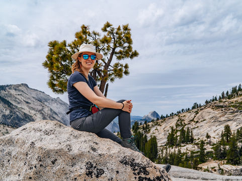 the author Claire sits on a rock at Olmstead point, with granite domes and Yosemite valley behind