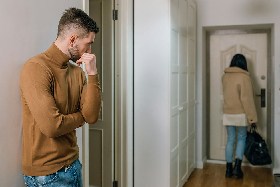 Man in brown sweater looks concerned as woman in beige coat walks toward a door, holding a bag. Indoor setting, neutral tones.