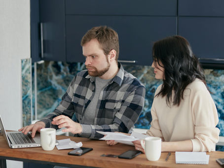 Man and woman at a table, focused on a laptop. Papers and mugs are present, set against a blue marble background, conveying concentration.