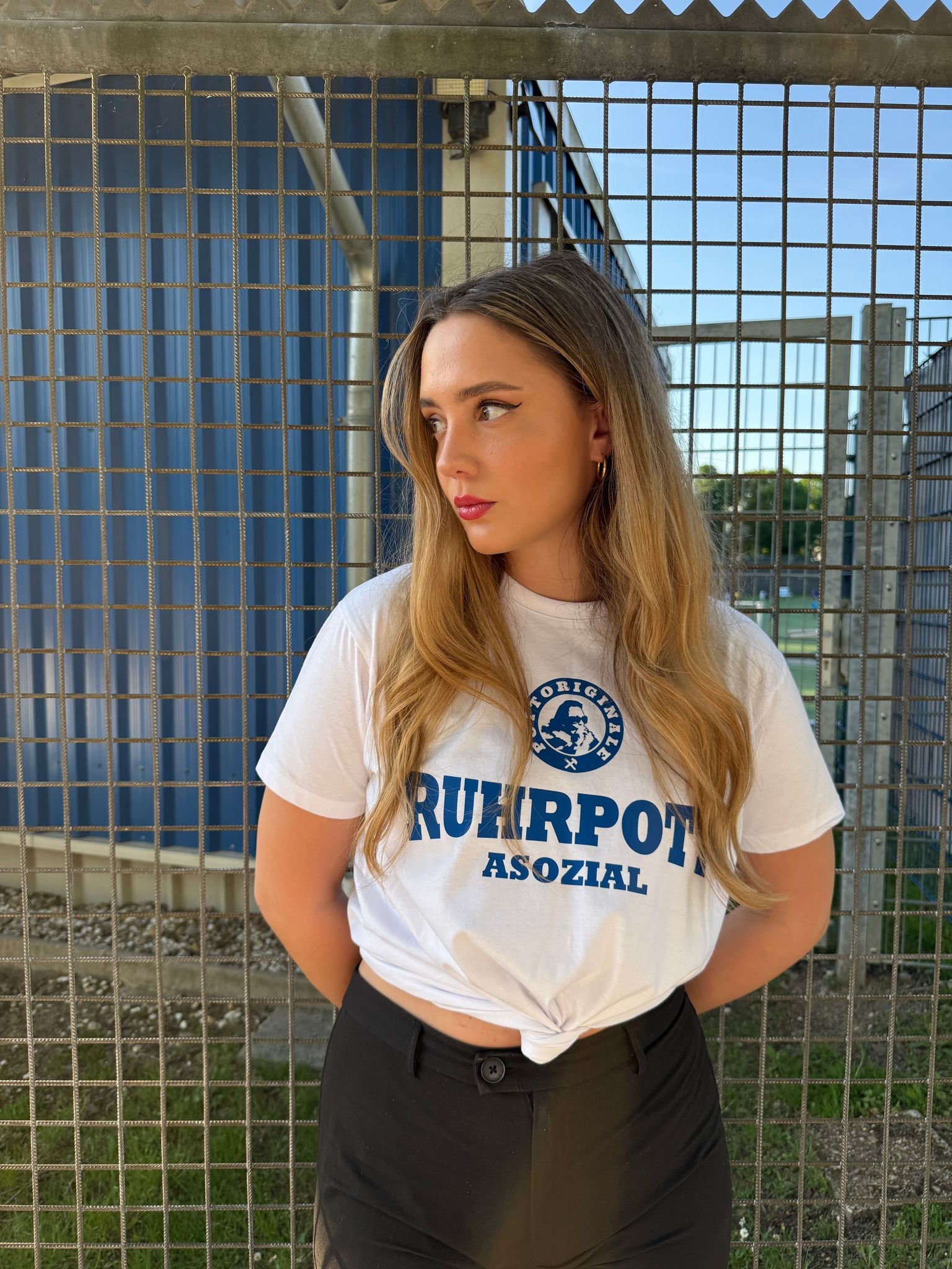 Junges blondes Mädchen mit einem kurzarm T-Shirt, vorne drauf steht "Ruhrpott Asozial" unter dem Pottoriginale Logo