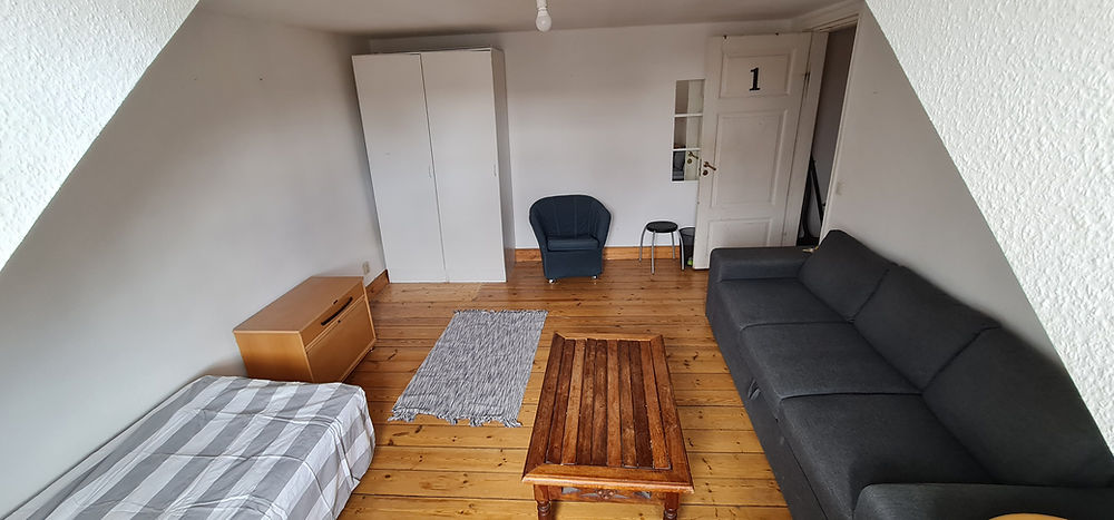 Furnished student housing room with bed, sofa, and wardrobe
