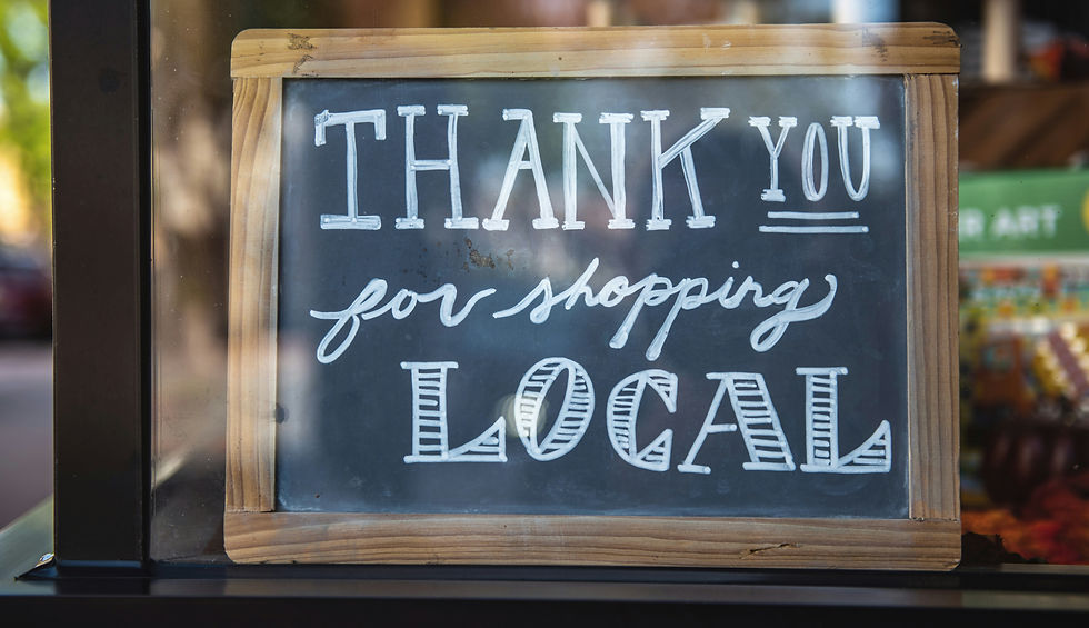 A charcoal slate stands in front of a display window with the words "Thank you for shopping local" written on it.
