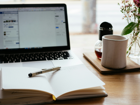 An open notebook with a pen placed on top in front of an open laptop showing a writing software document.