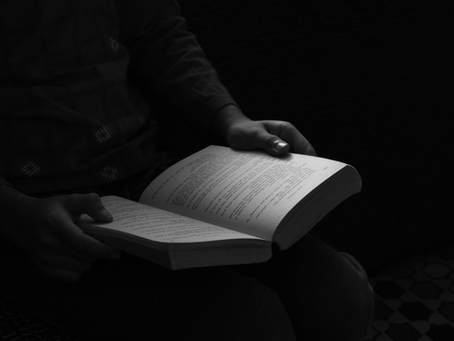 A black and white picture of a person holding an open book in the dark.