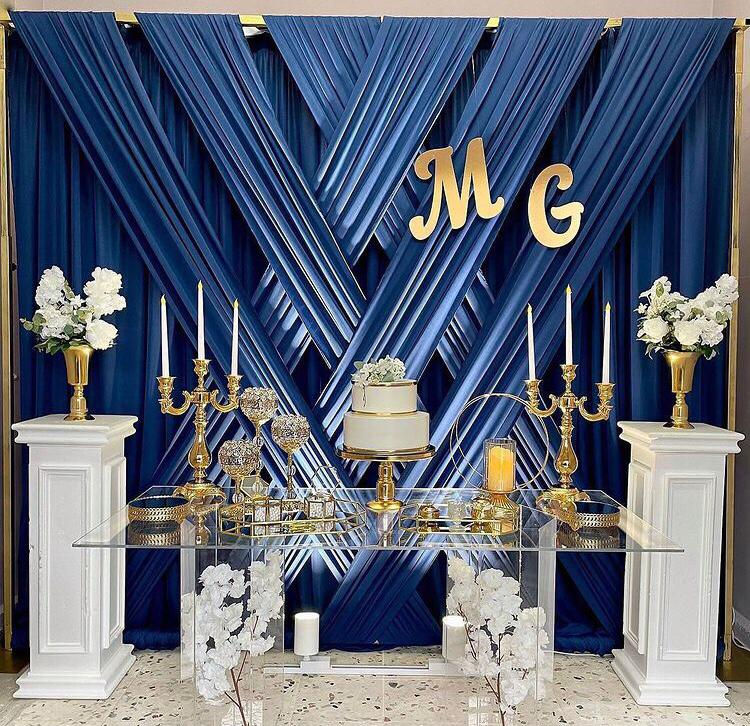 Düğün pastası, MG logosu, beyaz sütunlar, mavi perde arka planı, çiçekler, mum ve Tavsiye Benden