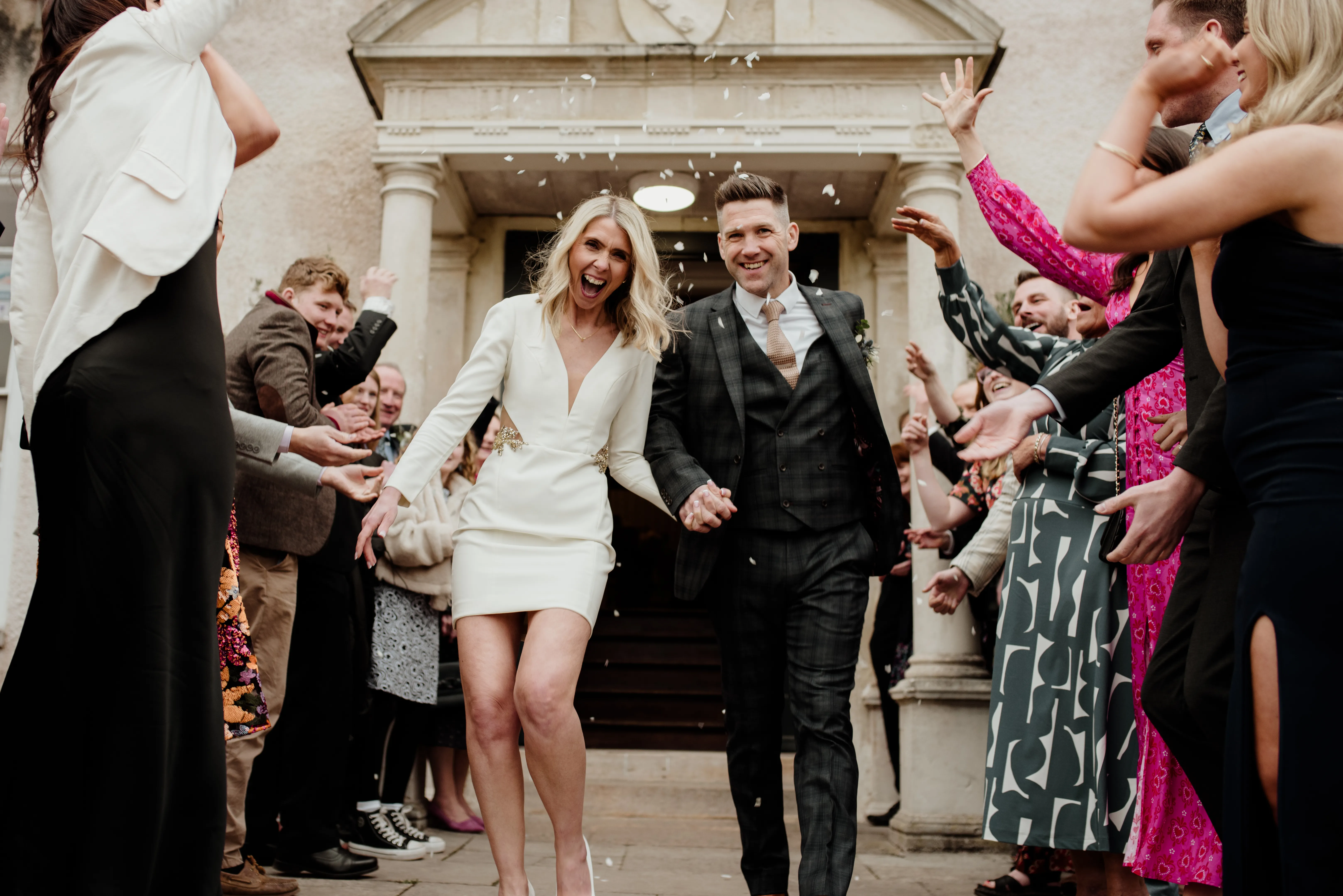 Ecstatic bride and groom leaving ceremony while guests throw confetti
